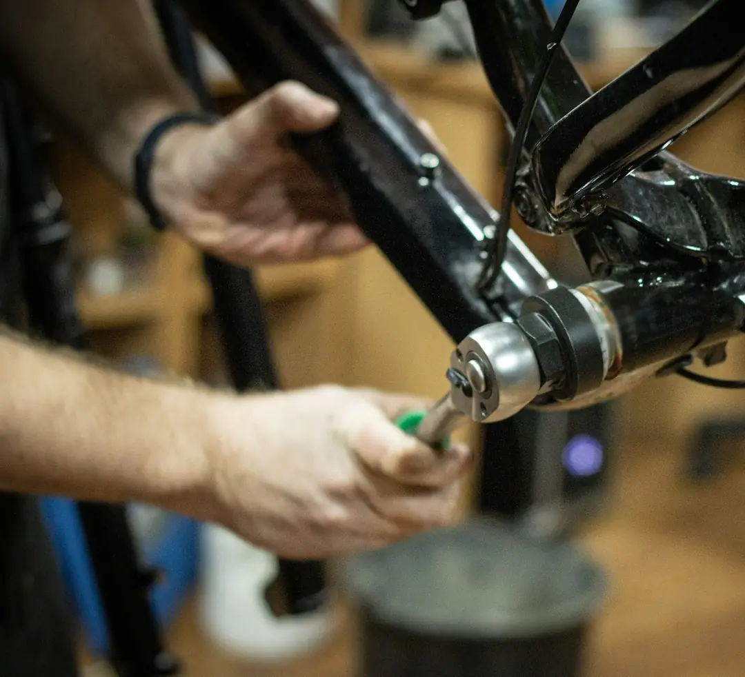 Hands fitting a bottom bracket to a black bike frame with a workshop tool.